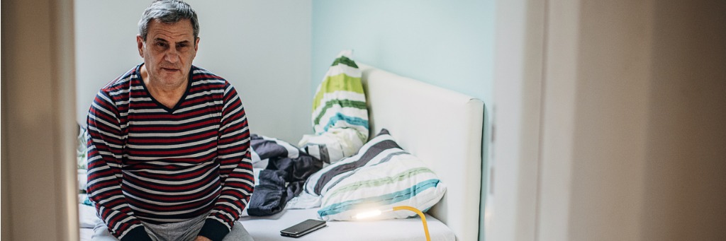 Man sitting on bed, striped shirt.